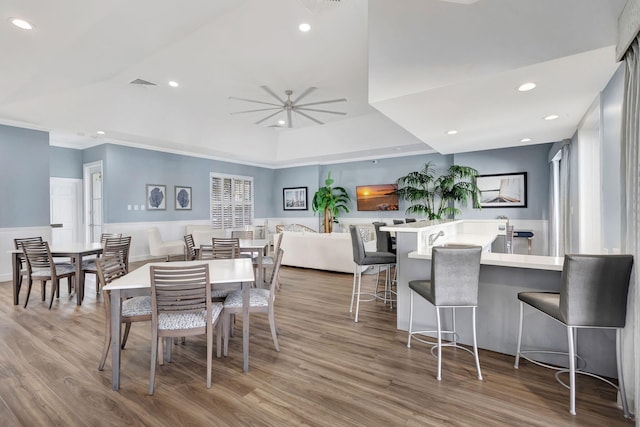 dining room featuring wood-type flooring, a raised ceiling, ceiling fan, and ornamental molding