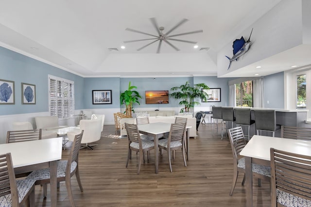 dining space with ceiling fan, a raised ceiling, dark wood-type flooring, and crown molding