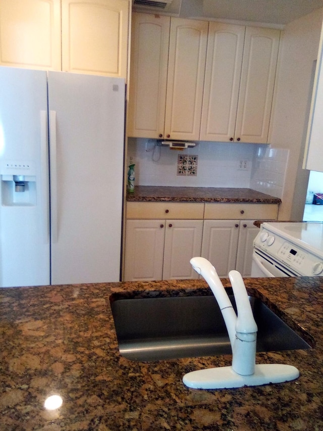 kitchen with dark stone counters, white appliances, white cabinets, and a sink