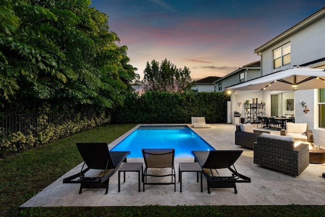 pool at dusk with outdoor lounge area and a patio