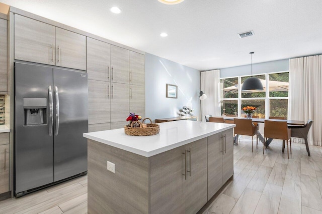 kitchen with stainless steel fridge with ice dispenser, a textured ceiling, a center island, and hanging light fixtures