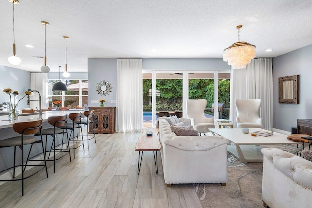 living room featuring a textured ceiling, light wood-type flooring, a healthy amount of sunlight, and a notable chandelier