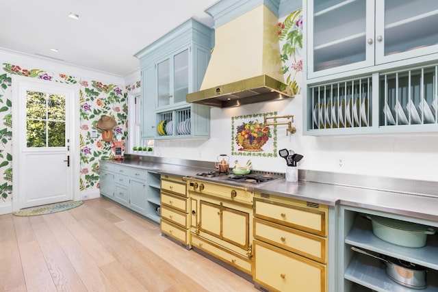 kitchen featuring stainless steel counters, wall chimney exhaust hood, stainless steel gas cooktop, light hardwood / wood-style floors, and ornamental molding