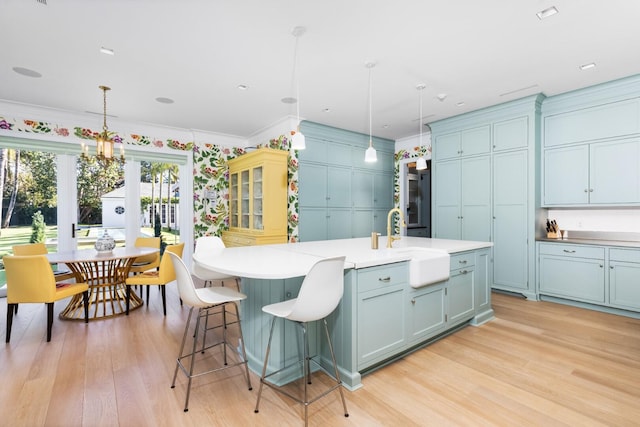 kitchen with decorative light fixtures, a center island with sink, light hardwood / wood-style floors, and crown molding