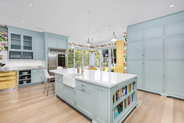 kitchen featuring a breakfast bar, sink, pendant lighting, stainless steel built in fridge, and an island with sink