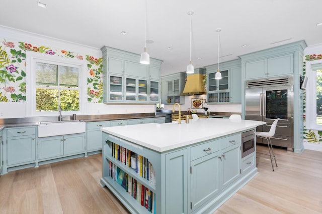 kitchen with pendant lighting, premium range hood, sink, built in appliances, and an island with sink