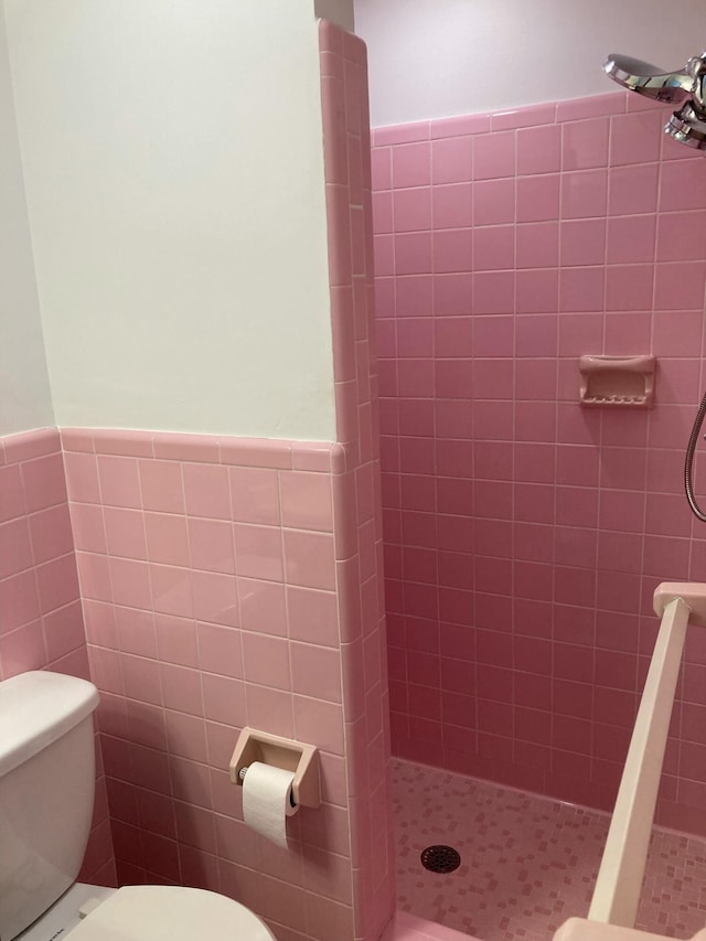 bathroom featuring tiled shower, toilet, and tile walls