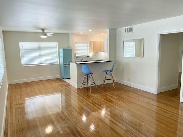 kitchen featuring backsplash, light hardwood / wood-style flooring, light brown cabinetry, kitchen peninsula, and a breakfast bar area