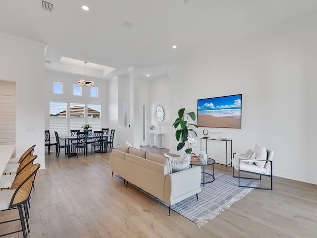 living room with a tray ceiling, light hardwood / wood-style flooring, a chandelier, and ornamental molding