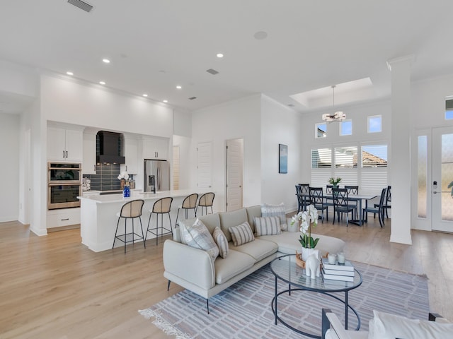 living room with ornamental molding, light hardwood / wood-style flooring, a high ceiling, and an inviting chandelier