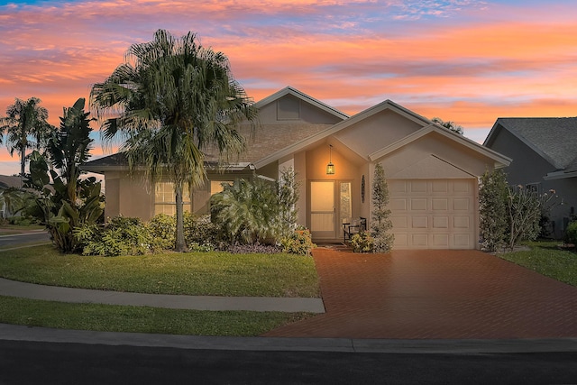 view of front of home with an attached garage, decorative driveway, a lawn, and stucco siding