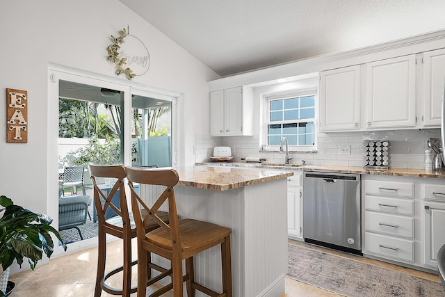 kitchen with lofted ceiling, stainless steel dishwasher, tasteful backsplash, and white cabinetry