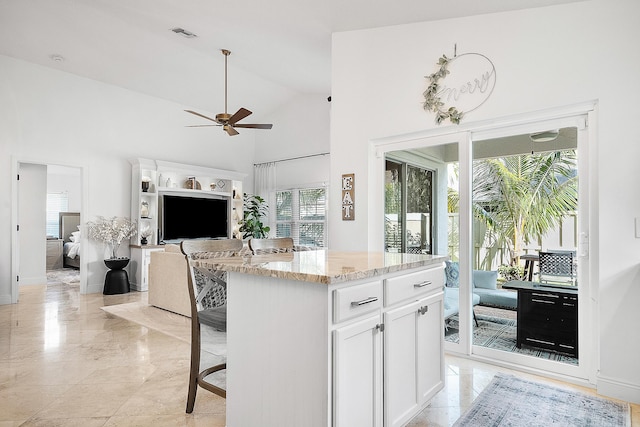 kitchen featuring light stone counters, a kitchen island, a breakfast bar area, white cabinets, and ceiling fan