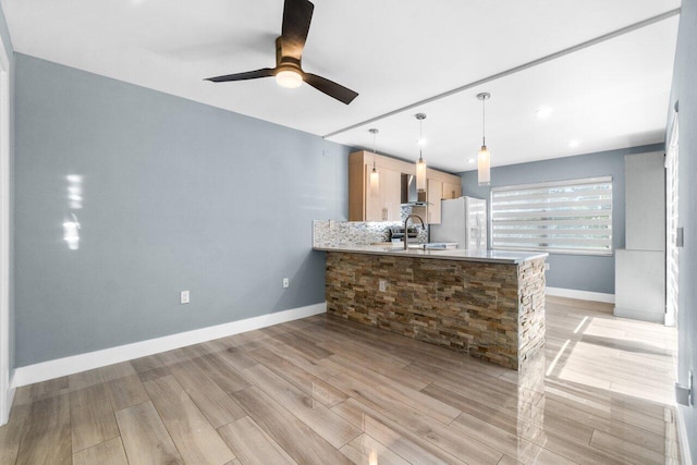 kitchen with kitchen peninsula, light brown cabinets, white fridge, and wall chimney range hood