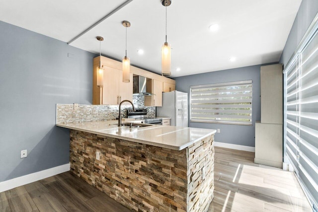 kitchen featuring kitchen peninsula, light brown cabinetry, light stone countertops, wall chimney range hood, and white fridge with ice dispenser