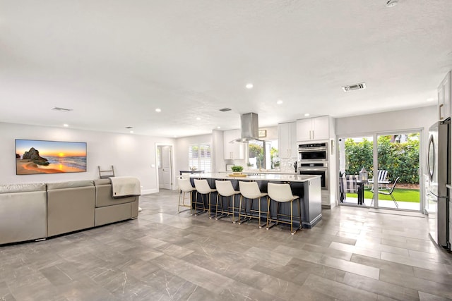 kitchen with a breakfast bar, island range hood, white cabinets, appliances with stainless steel finishes, and a kitchen island