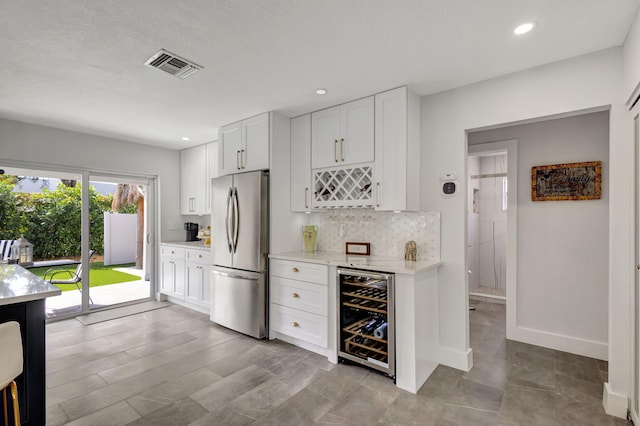 kitchen featuring backsplash, stainless steel refrigerator, white cabinets, and beverage cooler