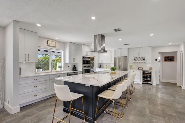 kitchen featuring a large island, wall chimney exhaust hood, beverage cooler, white cabinets, and appliances with stainless steel finishes