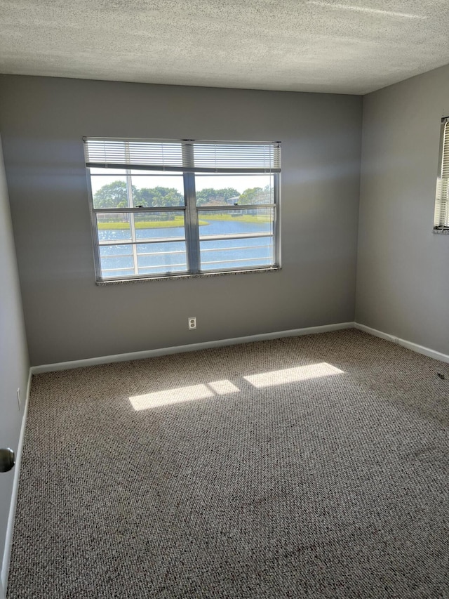 unfurnished room featuring carpet, a textured ceiling, and a water view