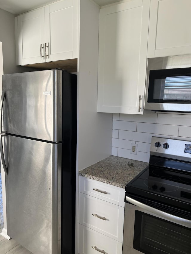 kitchen with tasteful backsplash, light stone countertops, white cabinets, and stainless steel appliances