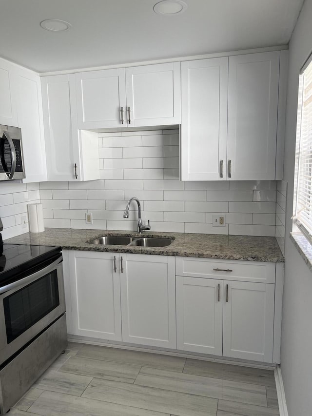 kitchen with stainless steel appliances, white cabinetry, dark stone countertops, and sink