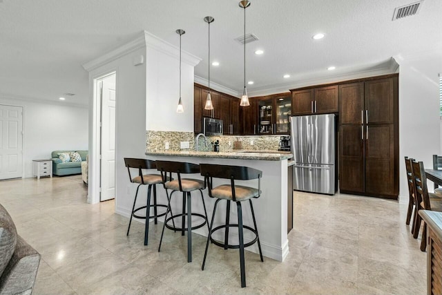 kitchen featuring ornamental molding, appliances with stainless steel finishes, decorative light fixtures, a kitchen bar, and kitchen peninsula