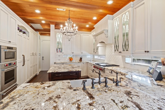 kitchen with light stone countertops, an inviting chandelier, white cabinets, appliances with stainless steel finishes, and wooden ceiling