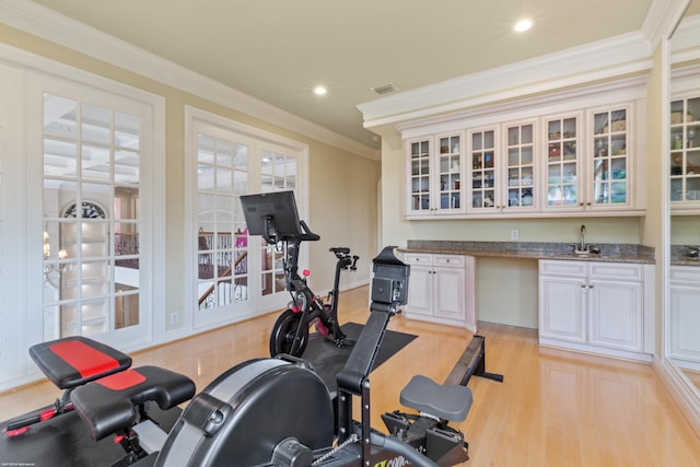 exercise area with visible vents, a sink, crown molding, light wood finished floors, and wet bar