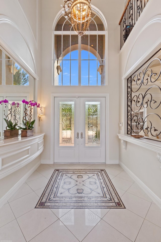 tiled entrance foyer with a notable chandelier, french doors, baseboards, and a towering ceiling