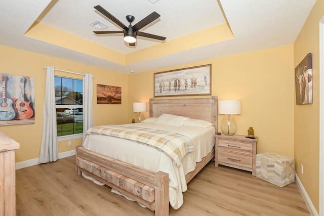 bedroom with light wood-type flooring, a tray ceiling, and ceiling fan