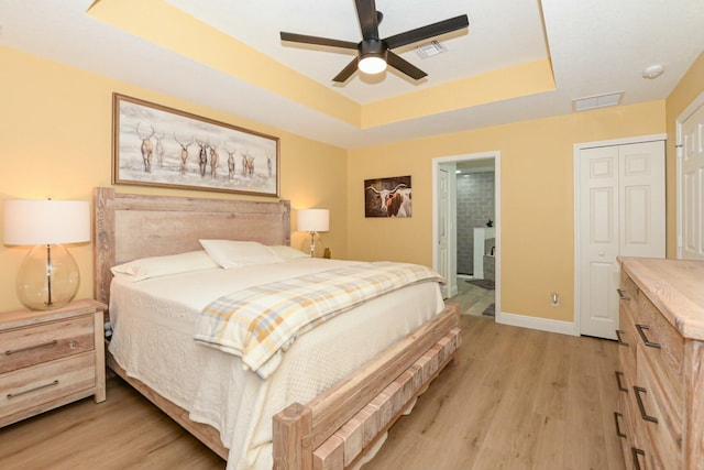 bedroom with a raised ceiling, ceiling fan, a closet, and light hardwood / wood-style floors