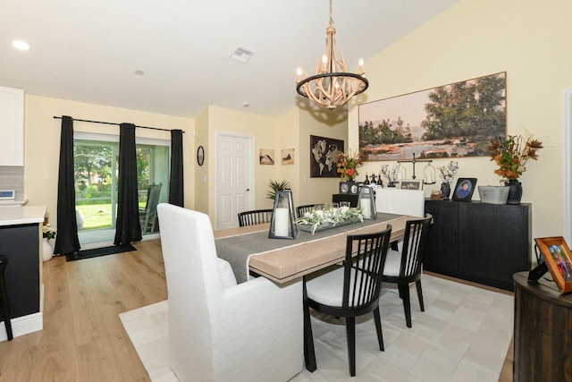 dining space with light hardwood / wood-style floors, an inviting chandelier, and lofted ceiling