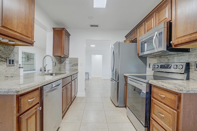 kitchen featuring decorative backsplash, appliances with stainless steel finishes, light stone counters, sink, and light tile patterned floors