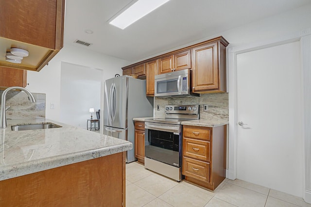 kitchen with light tile patterned flooring, stainless steel appliances, light stone countertops, and sink