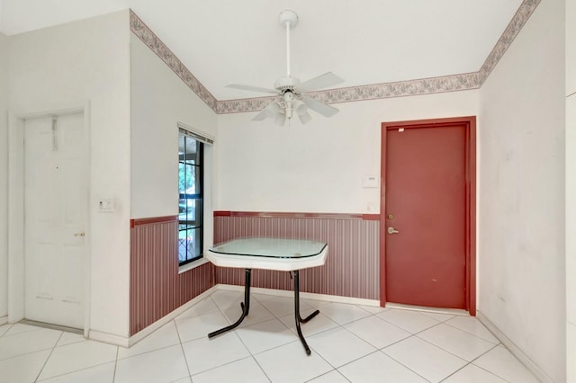 unfurnished dining area featuring tile patterned floors, a ceiling fan, and wainscoting