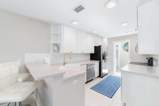 kitchen with a kitchen bar, appliances with stainless steel finishes, kitchen peninsula, sink, and white cabinets