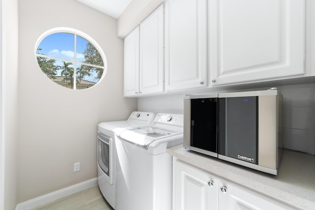 clothes washing area featuring washing machine and clothes dryer, light tile patterned floors, and cabinets