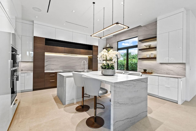 kitchen with white cabinets, backsplash, an island with sink, and hanging light fixtures