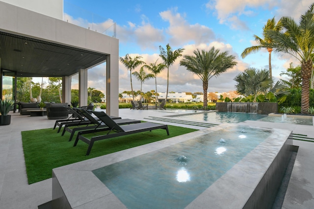 pool at dusk with pool water feature and a patio