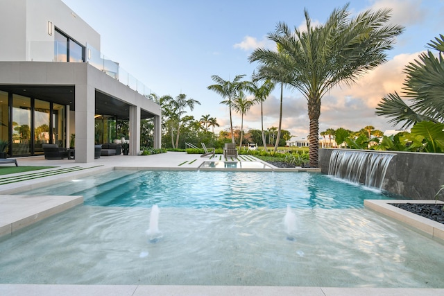 pool at dusk with pool water feature and a patio