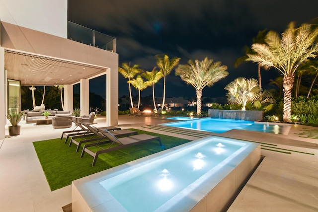 pool at night with an outdoor living space and a patio