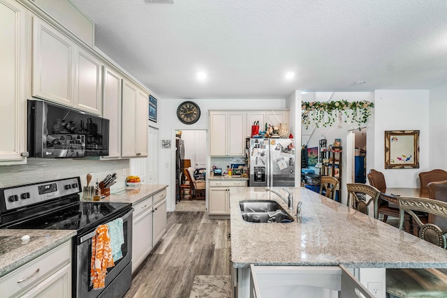 kitchen with light stone counters, sink, stainless steel appliances, and a kitchen island with sink