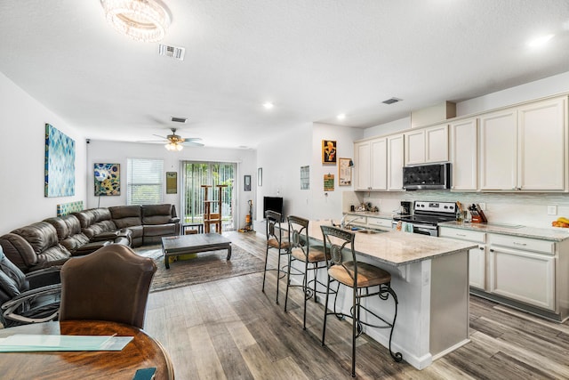 kitchen with a breakfast bar, a kitchen island with sink, hardwood / wood-style flooring, light stone countertops, and appliances with stainless steel finishes