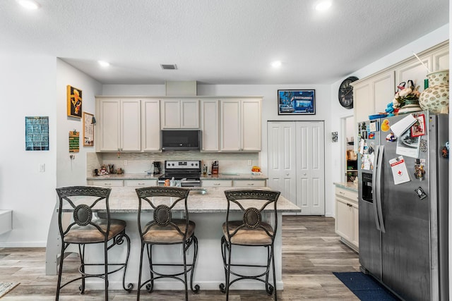 kitchen with backsplash, a center island with sink, light stone countertops, a kitchen bar, and stainless steel appliances