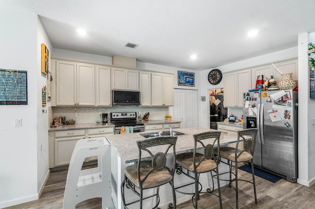 kitchen with light stone countertops, light hardwood / wood-style flooring, a breakfast bar area, a center island with sink, and appliances with stainless steel finishes