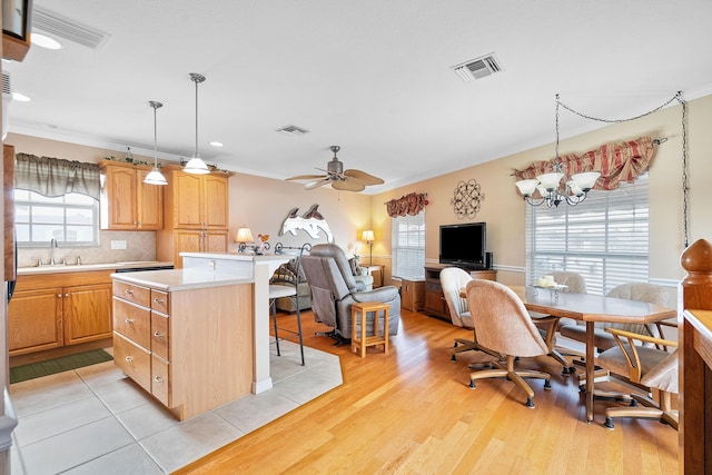 kitchen featuring backsplash, ceiling fan with notable chandelier, hanging light fixtures, light hardwood / wood-style flooring, and a kitchen island