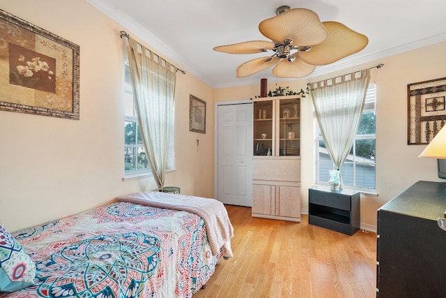 bedroom featuring ceiling fan, crown molding, light hardwood / wood-style flooring, multiple windows, and a closet