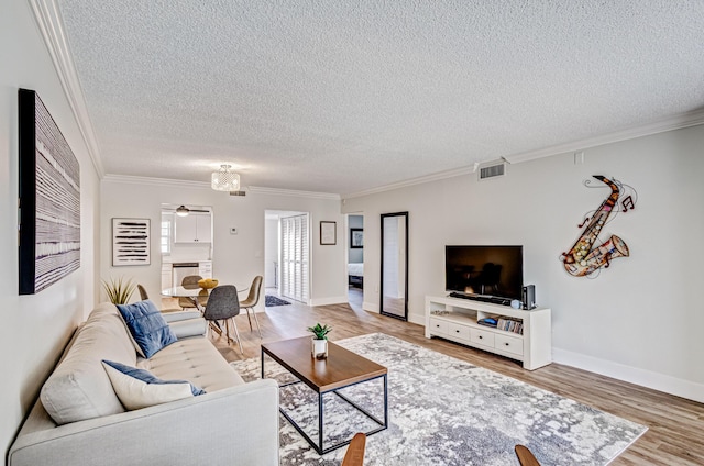 living room featuring a textured ceiling, light wood-style flooring, ornamental molding, a ceiling fan, and baseboards