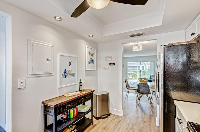 hall featuring electric panel, a tray ceiling, light wood-style floors, ornamental molding, and baseboards