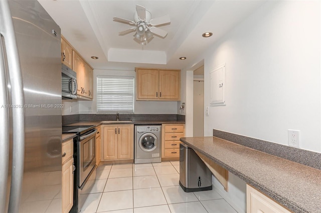 kitchen featuring washer / dryer, a tray ceiling, light brown cabinetry, light tile patterned floors, and appliances with stainless steel finishes